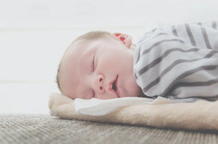 Baby dressed in white and grey stripes sleeping on fuzzy white blanket on the floor with white background