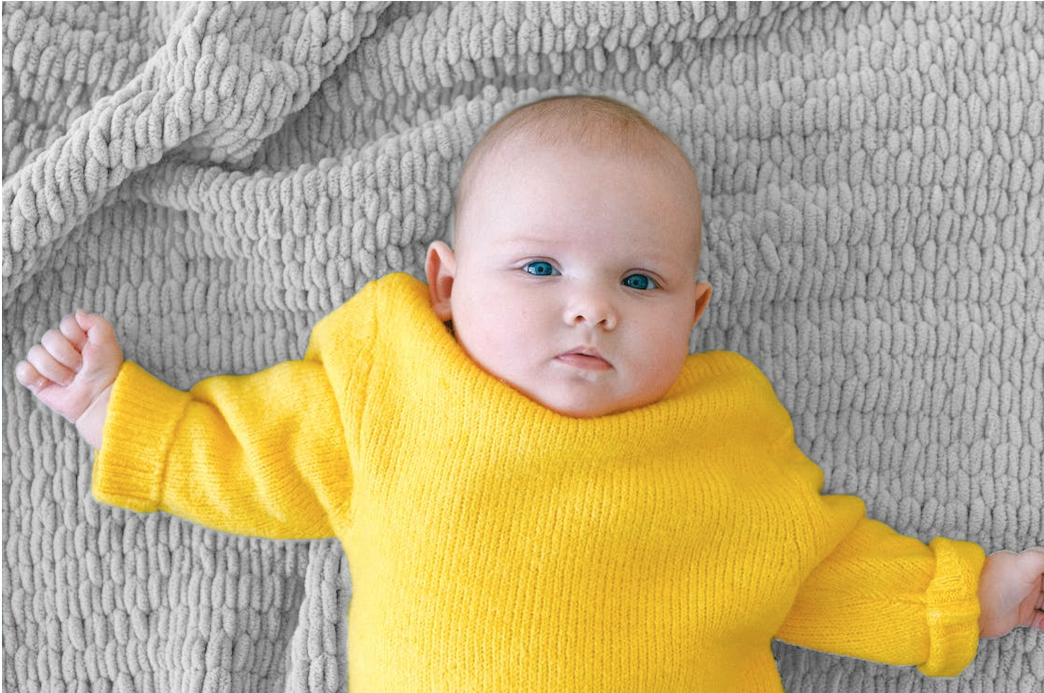 Baby wearing a yellow sweater lying on a light grey knit blanket